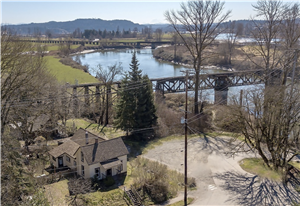 A small 1890s house next to a bridge that spans a river. Green fields and trees dot the landscape